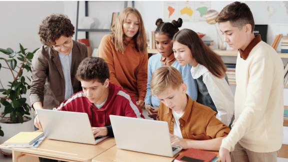 A photograph with 7 children of different nationalities in a school classroom with a laptop making a presentation