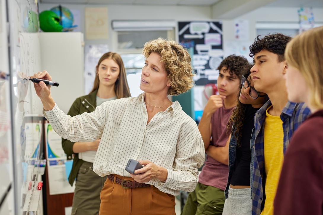 Teacher writing on a whiteboard while a group of students watches